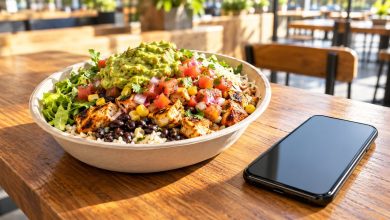 Burrito bowl with rice, beans, salsa and guacamole next to a phone on a sunny restaurant table