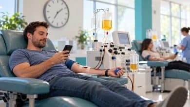 Donor relaxing in a reclining chair beside a plasma collection machine at a bright donation center, with a wall clock in the background