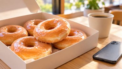 Box of glazed doughnuts with a cup of coffee and a smartphone on a cafe counter