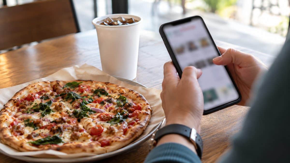 Person holding a smartphone next to a personal pizza and a fountain drink
