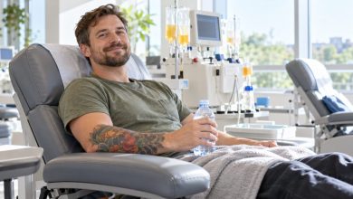 Plasma donor with a forearm tattoo relaxing in a donation chair holding a water bottle