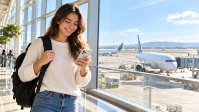 Smiling college student with a backpack checking her phone in a bright airport terminal with planes outside